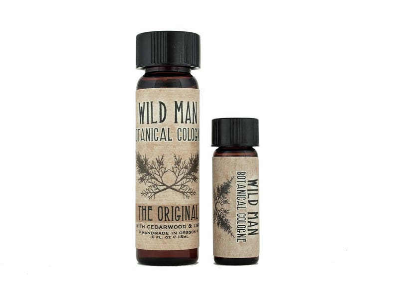 May include: Two amber glass bottles of Wild Man Botanical Cologne with black screw caps. The larger bottle label reads Wild Man Botanical Cologne, The Original, with Cedarwood & Lime, Handmade in Oregon, .5 fl. oz / 15ml. The smaller bottle label reads Wild Man Botanical Cologne.