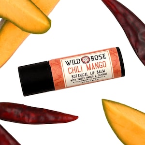 May include: A black and pink tube of Wild Rose Chili Mango Botanical Lip Balm with sweet mango and cayenne. The tube is surrounded by slices of mango and red chili peppers.