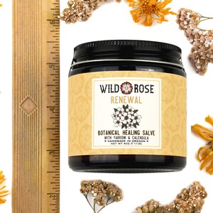 Renewal Healing Salve in a 4oz amber glass jar with metal lid. Shown near a ruler at about 3" tall. Dried yarrow and calendula surround.