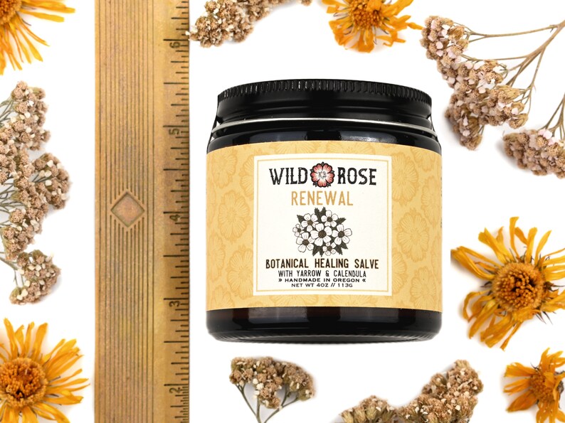 Renewal Healing Salve in a 4oz amber glass jar with metal lid. Shown near a ruler at about 3" tall. Dried yarrow and calendula surround.