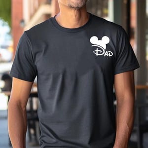 May include: Black t-shirt with a white Mickey Mouse head and the word "DAD" in a stylized font. The shirt is short-sleeved and appears to be made of a soft material.