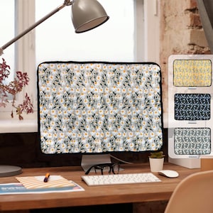May include: A computer monitor cover featuring a floral design of white daisies, yellow centres, and green leaves on a grey backdrop, with a black border. Three other covers with different floral patterns are shown.