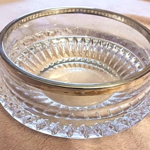May include: A clear glass bowl with a silver rim. The bowl has a decorative, cut-glass design around the base and on the interior. The bowl is likely for serving or display.