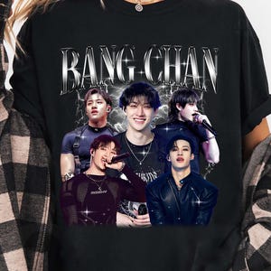 Peut inclure: T-shirt noir avec l'inscription "BANG CHAN" en argenté et vieilli. En dessous, un collage de cinq personnes. Les personnes portent différentes tenues et posent. Le graphisme a un aspect vintage.