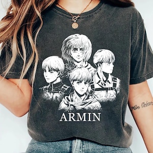 May include: Dark gray t-shirt featuring a white graphic of anime characters with the name "ARMIN" printed below. The design includes multiple portraits of the character Armin Arlert. The shirt has a vintage, worn look.