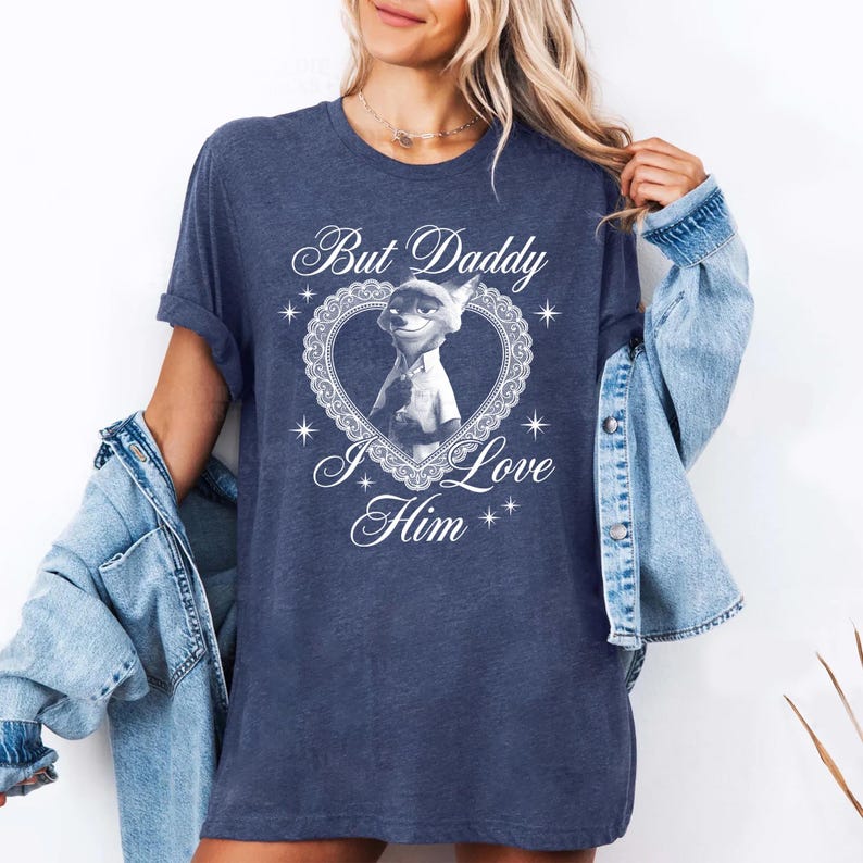 K&ouml;nnte beinhalten: Marineblaues T-Shirt mit einem Cartoon-Fuchs-Charakter in einem herzf&ouml;rmigen Design. Der Text "But Daddy I Love Him" steht &uuml;ber und unter dem Bild. Das T-Shirt hat kurze &Auml;rmel und eine lockere Passform.