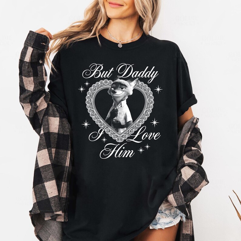 K&ouml;nnte beinhalten: Schwarzes T-Shirt mit einer Cartoon-Fuchsfigur in einem herzf&ouml;rmigen Rahmen. Der Text "But Daddy I Love Him" steht oberhalb und unterhalb des Bildes in einer dekorativen Schriftart. Das T-Shirt ist ein l&auml;ssiger Stil.