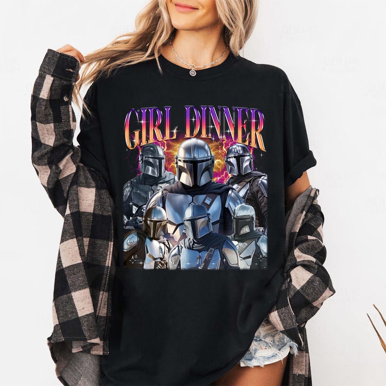 May include: Black t-shirt featuring a graphic of several Mandalorian characters with the text "GIRL DINNER" in a colorful, retro font. The design includes a purple and yellow lightning bolt effect behind the characters.