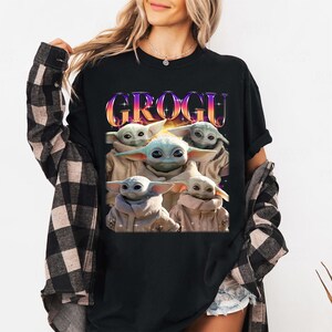 Może przedstawiać: Czarny t-shirt z grafiką Grogu, postaci z The Mandalorian. Słowo "GROGU" jest w kolorowej, gradientowej czcionce. Obraz przedstawia Grogu w beżowym płaszczu z dużymi uszami.