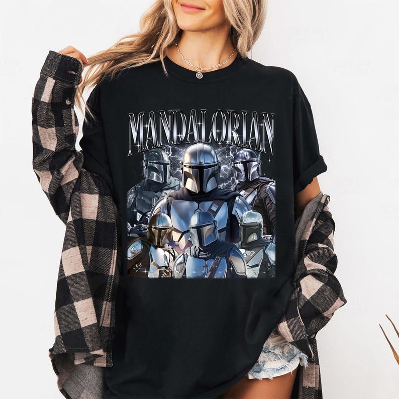 Pu&ograve; includere: T-shirt nera con una grafica di pi&ugrave; personaggi Mandaloriani in armatura argentata e grigia. La parola "MANDALORIAN" &egrave; stampata sopra i personaggi in un carattere argentato stilizzato.