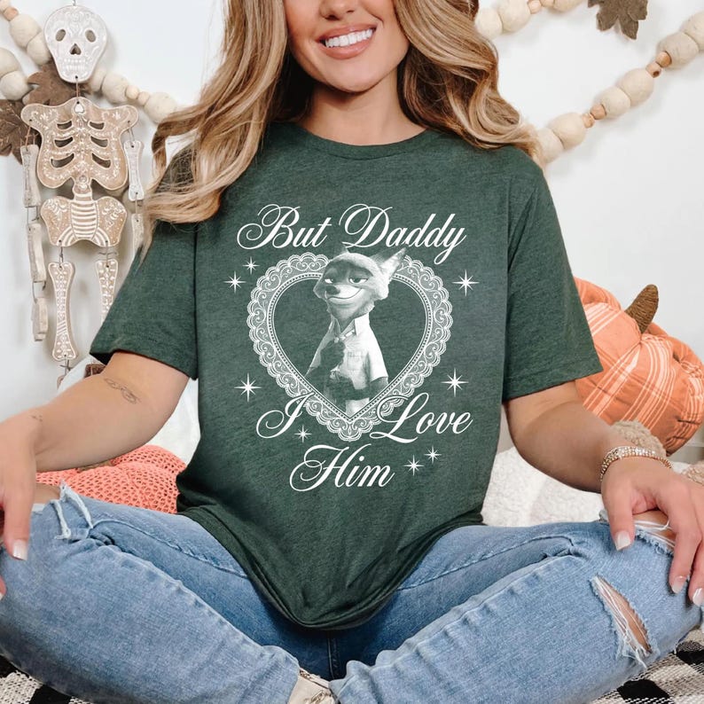 K&ouml;nnte beinhalten: Dunkelgr&uuml;nes T-Shirt mit dem wei&szlig;en Schriftzug "But Daddy I Love Him". Das Shirt hat ein herzf&ouml;rmiges Design mit einer Cartoonfigur. Die Person tr&auml;gt eine blaue Jeans.