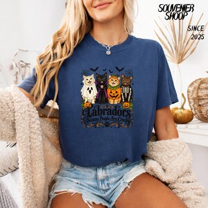 Peut inclure: Un t-shirt bleu marine avec un motif de quatre chats déguisés pour Halloween, incluant un fantôme, un vampire, une citrouille et un squelette. Le texte indique Labradors Because People Are Creepy. Le design inclut des chauves-souris.
