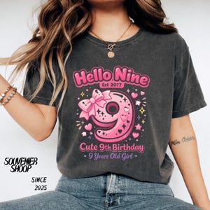 Peut inclure: T-shirt gris foncé avec un motif rose disant "Hello Nine" et "Cute 9th Birthday". Le chiffre 9 est rose avec un nœud et des cœurs. Le t-shirt dit aussi "9 Years Old Girl".