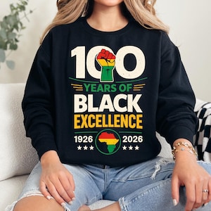 Peut inclure: Sweat-shirt noir avec l'inscription "100 YEARS OF BLACK EXCELLENCE" et les années 1926-2026. Le motif comprend un poing levé rouge, jaune et vert, ainsi qu'une carte de l'Afrique. Le sweat-shirt est à col rond.