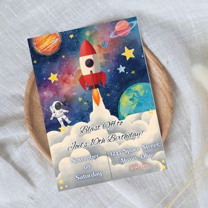 Puede incluir: Una invitación de cumpleaños con temática espacial. Presenta un cohete rojo despegando, un astronauta, planetas y estrellas sobre un fondo de galaxia en acuarela. El texto dice "Blast Off to Joel's 10th Birthday!" con fecha, hora y dirección.