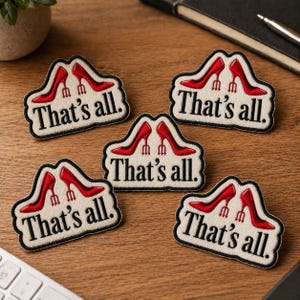 May include: Five embroidered patches with a cream background and black border. Each patch features a pair of red high heels and the text "That's all." The patches are arranged on a wooden surface.