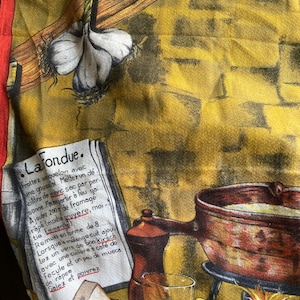 May include: A vintage fondue recipe printed on a yellow and brown fabric. The image features a garlic bulb, a fondue pot, a glass of wine, and a pepper grinder. The recipe is in French.