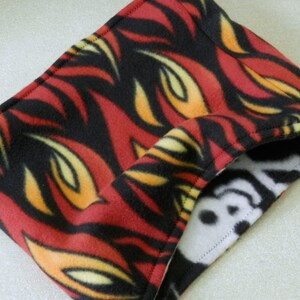 May include: A red, black, and yellow fleece neck warmer with a flame pattern. The neck warmer is reversible and has a white fleece side with a black and white pattern.
