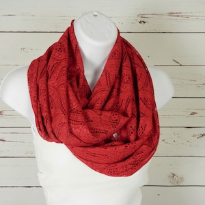 May include: A red knitted infinity scarf with a lacy pattern. The scarf is draped around a white mannequin.