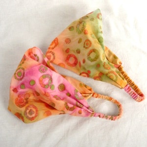 Könnte beinhalten: Zwei bunte Stirnbänder mit einem Batik-Muster in Rosa-, Orange- und Grüntönen. Die Stirnbänder haben elastische Bänder für einen bequemen Sitz.