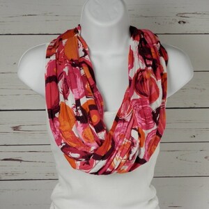 May include: A pink, orange, and white infinity scarf with a circular pattern. The scarf is made of a soft, stretchy fabric.