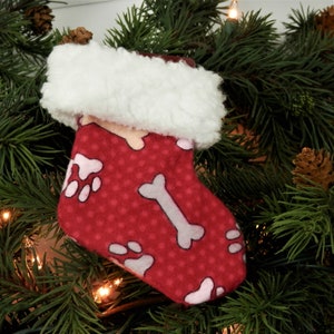 May include: Red Christmas stocking with a white faux fur cuff. The stocking is decorated with a white polka dot pattern and paw prints and bone designs.