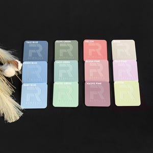 May include: A collection of square acrylic color samples in various pastel shades, including blue, green, pink, and beige. Each sample has rounded corners and is labeled with its color name and the word "Acrylics".