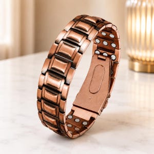 May include: A copper-toned link bracelet featuring a series of rectangular segments with a brushed finish. The interior of the bracelet displays a row of small, circular silver-colored magnets embedded within each link and a metal clasp closure.