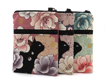 Puede incluir: Tres bolsos bandolera rectangulares con la silueta de un gato negro rodeada de grandes motivos florales en tonos rosa, morado, azul y crema. Cada bolso tiene un cierre de cremallera negro en la parte superior y un bolsillo horizontal con cremallera.
