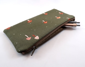 Puede incluir: Un estuche rectangular de color verde oliva con cremallera que presenta un patrón repetitivo de pequeñas setas naranjas y blancas con diminutos puntos blancos. El estuche está entreabierto, mostrando un bolígrafo gris oscuro y uno oro rosa.
