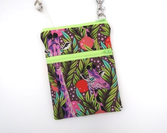 Puede incluir: Un bolso bandolera rectangular con fondo marrón oscuro y un estampado de jirafas moradas, hojas verdes y formas circulares rojas. El bolso cuenta con una cremallera de color verde lima brillante y una correa ajustable a juego.