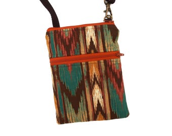 Puede incluir: Un bolso bandolera rectangular con un vibrante estampado ikat en tonos verde azulado, naranja óxido y marrón oscuro. El bolso incluye un bolsillo frontal horizontal con cremallera en color naranja óxido y una correa negra ajustable.