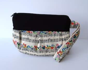 Puede incluir: Una bolsa de tela en blanco y negro con estampado floral y notas musicales. La bolsa tiene una cremallera negra y una correa negra.