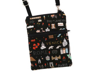 Puede incluir: Un bolso bandolera negro con un estampado de temática viajera que incluye ilustraciones de monumentos y los textos RIO DE JANEIRO, VENICE, ROME y PARIS. El bolso cuenta con un bolsillo frontal con cremallera, un compartimento principal y una correa negra ajustable.