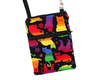 Puede incluir: Un bolso bandolera rectangular con base de tela negra y un estampado de gatos con degradado de arcoíris. El bolso incluye un bolsillo frontal con cremallera, un compartimento principal con cremallera y una correa negra ajustable con clip metálico.