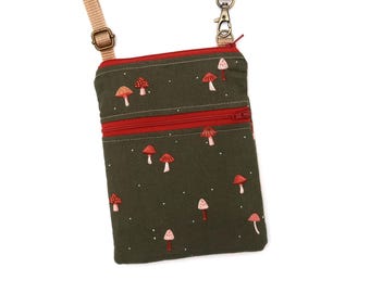 Puede incluir: Un bolso bandolera rectangular de color verde oliva con un patrón repetitivo de pequeñas setas rojas y rosas con puntos blancos. El bolso incluye un bolsillo frontal con cremallera roja, un cierre superior de cremallera roja y una correa ajustable de tela beige.