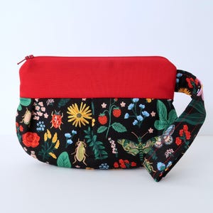 May include: A red and black zippered pouch with a floral print featuring butterflies, ladybugs, and flowers. The pouch has a red top flap and a black strap.