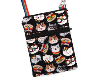 Puede incluir: Un bolso bandolera negro con un patrón repetitivo de caras de gatos de dibujos animados que llevan gafas y accesorios con los colores del arcoíris. El bolso incluye un bolsillo frontal con cremallera y una correa extraíble a rayas.
