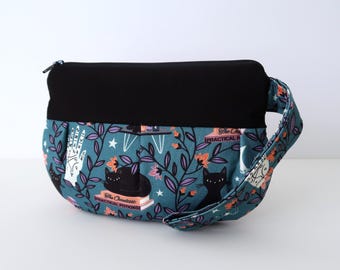 Puede incluir: Una bolsa de tela azul turquesa con una cremallera negra y una parte superior de tela negra. La bolsa tiene una correa negra y un estampado de gatos negros, estrellas y el texto "The Occultest Practical Potions".