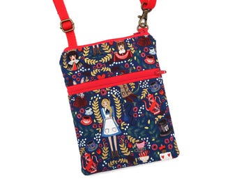 Puede incluir: Un bolso bandolera rectangular de tela azul marino con un patrón repetitivo de personajes de Alicia en el país de las maravillas, teteras y motivos florales. El bolso incluye una cremallera roja brillante, ribetes rojos y una correa ajustable.