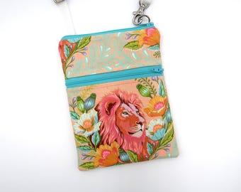 Puede incluir: Un bolso bandolera rectangular de tela color melocotón con un león estampado rodeado de flores y follaje de colores. El bolso incluye un bolsillo frontal con cremallera en color turquesa, una cremallera principal a juego y una correa blanca ajustable.