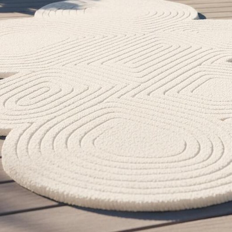 Puede incluir: Una alfombra de color crema con una superficie texturizada y acolchada que presenta un patr&oacute;n repetitivo de formas rectangulares redondeadas conc&eacute;ntricas. La alfombra tiene un aspecto suave y afelpado con l&iacute;neas en relieve.