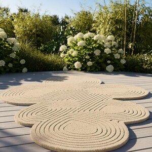 Puede incluir: Una alfombra beige de forma org&aacute;nica e irregular con una superficie texturizada de patrones conc&eacute;ntricos circulares y ovalados en relieve, que crean un efecto topogr&aacute;fico y superpuesto en toda la pieza de decoraci&oacute;n.