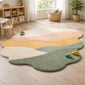 May include: An irregularly shaped area rug featuring a layered, wavy landscape design in muted tones of sage green, mustard yellow, peach, and cream. The rug has a textured, plush pile surface and is positioned on a light-colored wooden floor.