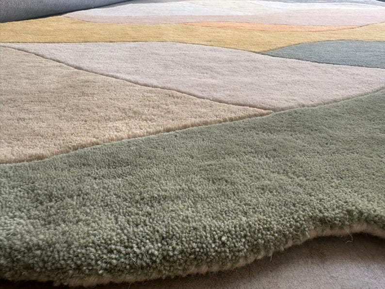 May include: A tufted area rug featuring an abstract pattern of organic, flowing shapes in muted tones of sage green, soft beige, pale pink, mustard yellow, and slate gray. The rug has a thick, textured pile with a soft, plush surface appearance.