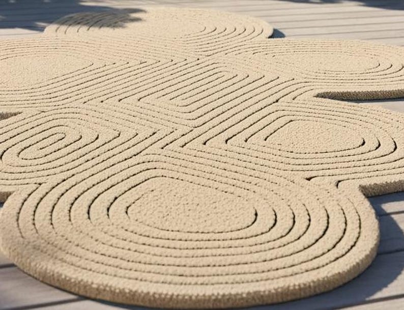 Puede incluir: Una alfombra de color beige con una superficie texturizada que presenta un patr&oacute;n repetitivo de c&iacute;rculos conc&eacute;ntricos y formas geom&eacute;tricas redondeadas. La alfombra tiene una construcci&oacute;n de pelo grueso con surcos profundos.