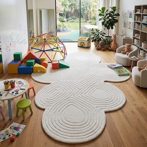 Puede incluir: Una alfombra grande de color blanco roto con un patr&oacute;n texturizado, conc&eacute;ntrico y similar a una nube que cubre el centro del suelo de una sala de juegos. La alfombra presenta l&iacute;neas redondeadas en relieve que forman formas org&aacute;nicas.