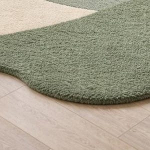 May include: A textured area rug featuring an organic, curved shape with a deep sage green section and a contrasting cream-colored section. The surface has a thick, plush, and curly pile construction that creates a soft, tactile appearance.