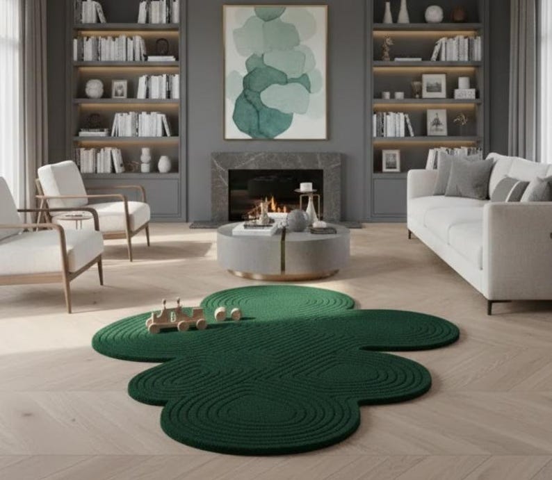 Puede incluir: Una alfombra de color verde oscuro con una forma org&aacute;nica irregular similar a una nube y un patr&oacute;n texturizado de c&iacute;rculos conc&eacute;ntricos. La alfombra est&aacute; colocada sobre un suelo de madera clara en una habitaci&oacute;n con chimenea, estanter&iacute;as y asientos.