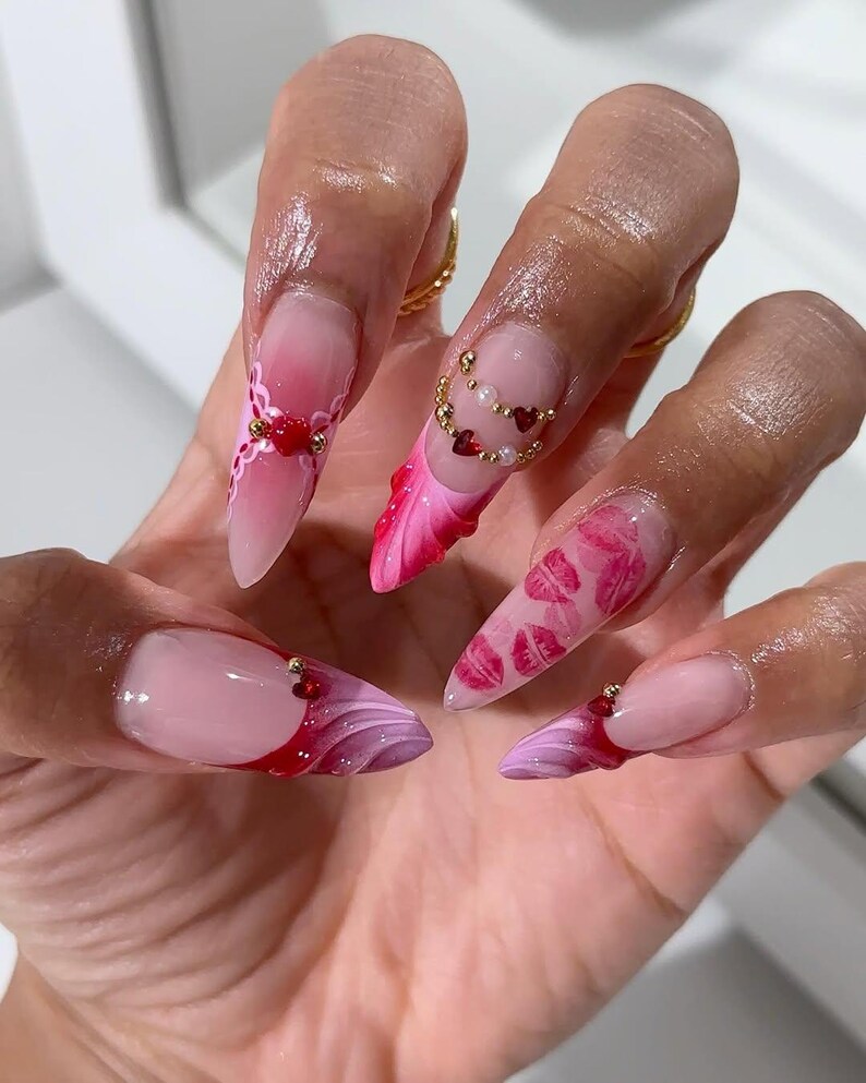 May include: Close-up of long, pointed acrylic nails with various designs. One nail features a French tip with a red and purple swirl, while others showcase pink gradients, heart and bead accents, and intricate patterns. The nails are a mix of pink, red, and white.